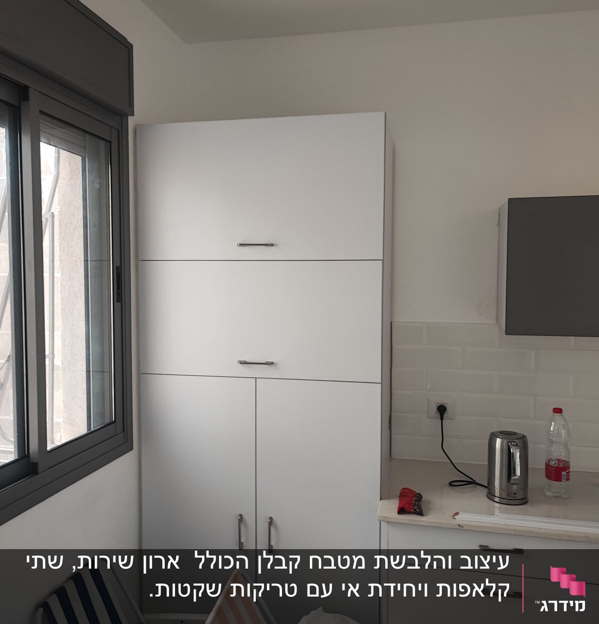 מטבח עם ארונות לבנים, קומקום חשמלי ובקבוק פלסטיק